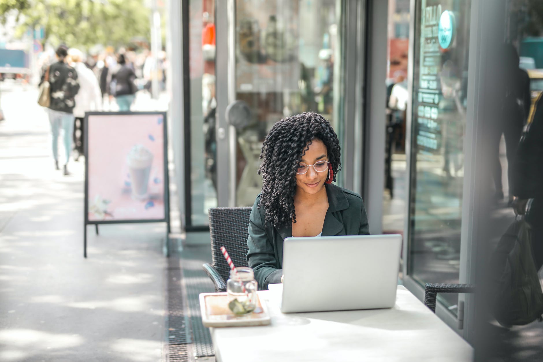 fashion blogger using laptop while having tasty beverage in modern street cafe